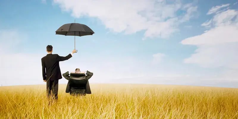 umbrella held over reclining businessman in a field